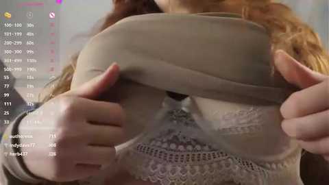 Media: A video of a light-skinned woman with curly red hair lifting a beige sweater to reveal white lace lingerie. Background shows a pink heart and a digital interface displaying numbers and icons.