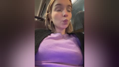 Media: Video of a young Caucasian woman with fair skin, light brown hair, wearing a purple sweater and black cardigan, making a pouty face.