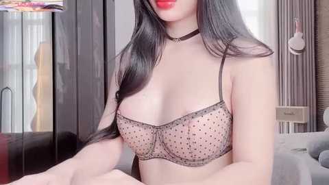 Media: Video of an Asian woman with long black hair, wearing a sheer, black polka-dot bra revealing her medium-sized breasts, standing indoors in a modern, well-lit room.