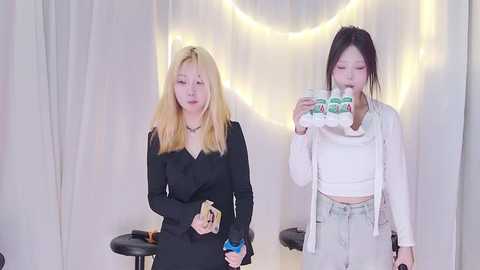 Media: Video of two Asian women with long, straight hair, one blonde, one black, dressed in black and white, holding food, against a white backdrop with fairy lights.