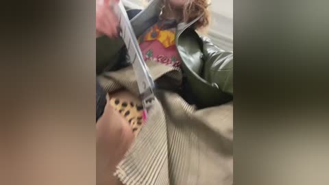 A video captures a woman in a green jacket, pink shirt, and leopard-print skirt, cutting a plastic bag with scissors, indoors, blurred background.