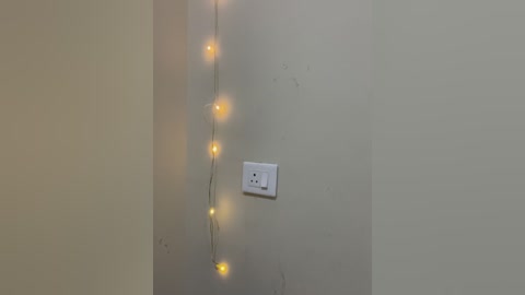 Media: A video of a plain beige wall with a white power outlet and a string of warm yellow fairy lights, creating a cozy ambiance.