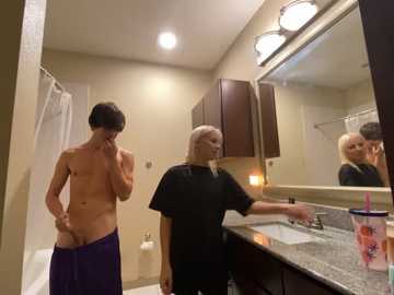 Media: Video of a blonde woman in a black shirt and a man in a purple towel, standing in a bathroom with a granite countertop, mirror, and white towels.