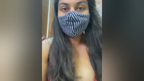 Media: A video of a young woman with long, dark hair, wearing a blue and white striped face mask, and a red bra, standing indoors.