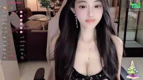 Media: A video of an Asian woman with long black hair, wearing a black sequined dress, and silver earrings, sitting in a modern living room with a couch and potted plants in the background.