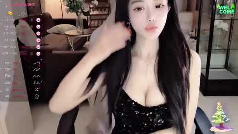 Media: Video of an East Asian woman with long black hair, wearing a black sequined dress, sitting in a modern living room, holding her hair.