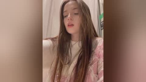 Media: A video of a young woman with long, wet brown hair, wearing a white top and pink floral robe, standing in a bathroom with a white shower curtain.