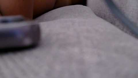 A close-up video of a person's head resting on a soft, grey blanket. The person's skin tone is light, and a cellphone is partially visible in the top left corner. The background is blurred, focusing on the blanket's texture and the person's relaxed posture.