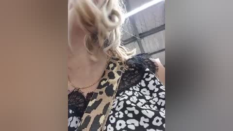 Video of a blonde woman with wavy hair, wearing a leopard print top, standing next to a person in a black-and-white leopard print dress, inside a dimly lit, industrial building with exposed ceiling.