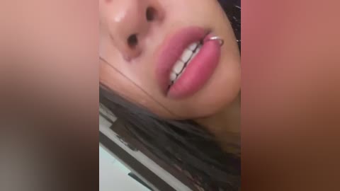 Media: Video of a close-up of a woman's face with light brown skin, wearing a silver nose ring, full lips painted in dark pink lipstick, and dark hair visible in the background.