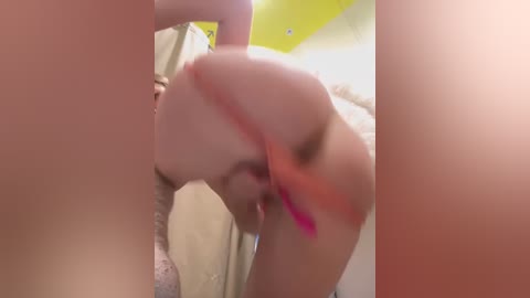 Media: Video of a blonde woman with pink hair, wearing a bra, bending over, with a blurred background.