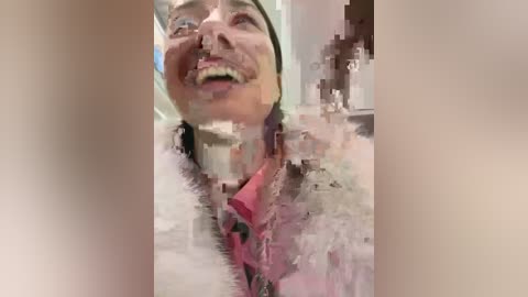 Media: Video of a woman with light skin and dark hair, laughing joyfully, wearing a pink shirt and white jacket. Background is blurred and pixelated, creating a surreal, glitchy effect.