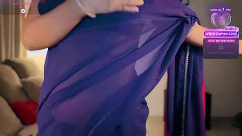 Media: Video of a person in a purple saree, showing the garment's semi-transparent fabric and pleats, taken indoors with a blurred background of a living room.