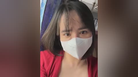 Media: Video of an Asian woman with shoulder-length black hair, wearing a white surgical mask, a red top, and a blue background.