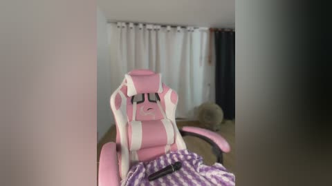 Media: Video of a pink gaming chair with a distressed, sleep-deprived expression, draped in a purple and white striped blanket. Background features a beige carpet, white curtains, and a dark curtain.