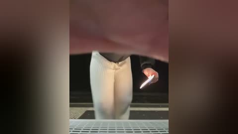 Media: A video of a person in white pants and a black sweater, holding a phone, standing on a grate, blurred background.