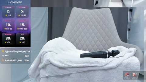 Media: A video shows a plush, quilted white armchair with a black sex toy and white blanket, set against a sleek, modern gray background.