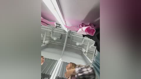 Video of a dimly lit airplane lavatory showing a person with a light brown jacket, a pink handbag, and a pink towel hanging above.