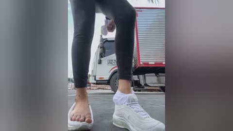 Media: Video of a person wearing black leggings and white sneakers, with a white van and red trailer in the background.