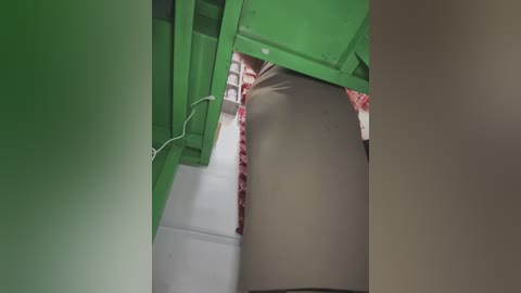 A video showing a person's lower legs and feet inside a green, industrial-looking machine with a beige, cylindrical drum. The person is wearing black shoes and a white sock. The background shows a red and white patterned surface.