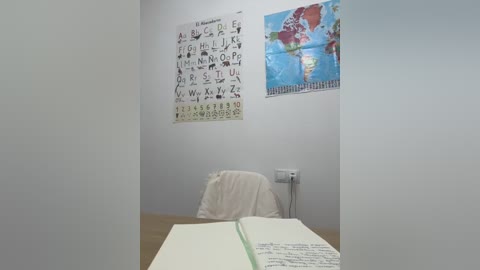 Media: Video of a small, sparsely decorated classroom with a whiteboard, alphabet poster, and a desk with an open book and a white jacket.