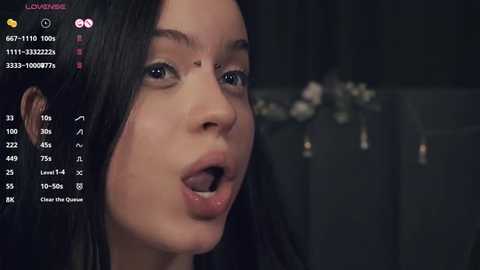 Media: Video of a young woman with long black hair, wearing a black top, captured in a close-up, open-mouthed expression, against a blurred dark background, with a video call interface visible.