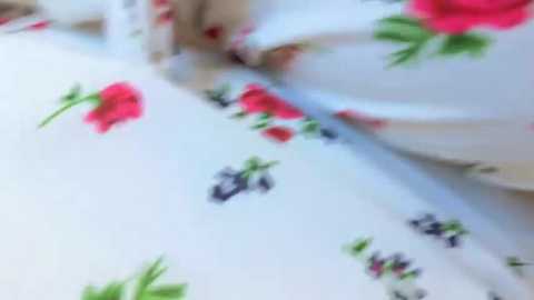 Media: A video of a white bedsheet with a floral pattern featuring red poppies, green leaves, and black text, possibly \"PANDORA.\" The bed is made, and the focus is on the bedspread.