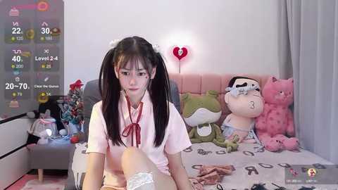 Media: A video shows an East Asian girl with pigtails, wearing a pink school uniform, sitting on a bed with stuffed toys, in a room with a pink heart light.