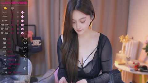 Media: Video of a young Asian woman with long black hair, wearing a sheer black top, sitting at a desk, surrounded by a cozy, dimly lit room with a Christmas tree and decorations.