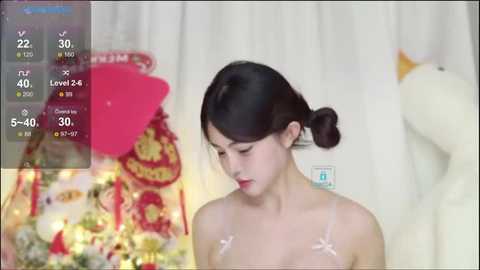 Media: A video of an East Asian woman with fair skin and dark hair in a bun, wearing a pink bra. She stands in front of a white curtain with a stuffed yellow duck. The image includes a virtual reality interface with health stats.