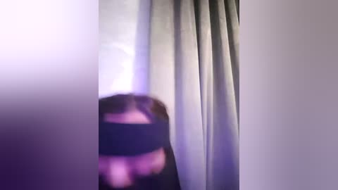 Media: A video captures a blurred figure in a dark outfit standing behind a sheer, light-colored curtain, creating a soft purple glow from the light behind them.