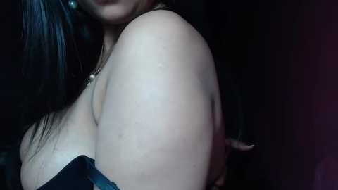 Media: A close-up video of a woman with pale skin, large breasts, and dark hair. She is wearing a black, strapless top, partially visible. The background is dark and indistinct, emphasizing the subject's features.