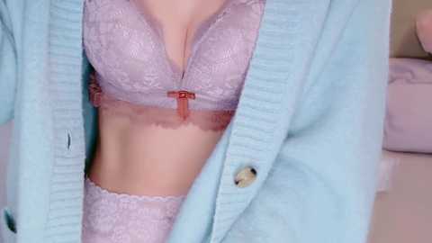 Media: Video of a woman's torso in light lavender lace lingerie, including a bra with a small red bow and matching panties. She wears a light blue cardigan, her skin is light-toned, and the background is soft and neutral.