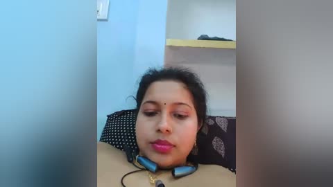 Media: A video shows a woman with dark hair and a bindi, wearing headphones, lying on a bed with a patterned pillow and white walls.