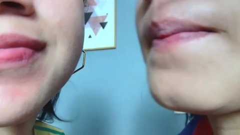 Media: Video of two close-up portraits of women's lips, showing lipstick variation. One has pink lips with a glossy finish, while the other has a matte nude shade. Background features a geometric abstract art piece and light blue wall.