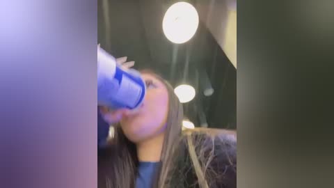 A blurry video of a woman drinking from a blue can, her long hair partially covering her face, in a dimly lit car.