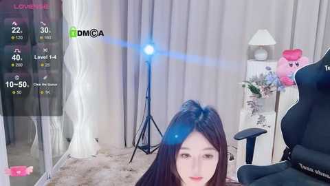 Media: A video of a young Asian woman with long black hair, sitting in a black gaming chair, streaming on Twitch. The room features a white lamp, a plush toy, and a backdrop of white curtains.