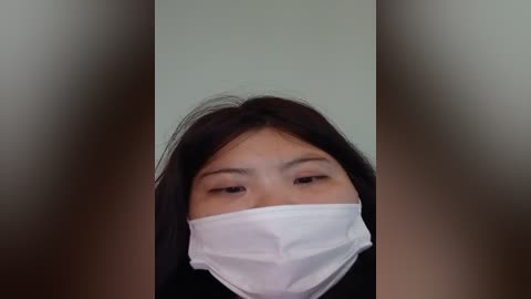 Media: A video of a woman with long black hair, wearing a white surgical mask, taken from a low angle, with blurred vertical lines in the background.