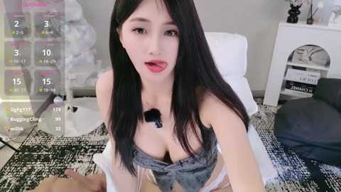 Media: A video of a young East Asian woman with long black hair, wearing a low-cut denim top, lying on a bed with a white pillow.