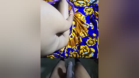 Media: Video showing a close-up view of a person's bare buttocks and thighs, partially covered by a vibrant, patterned fabric with yellow and blue flowers.