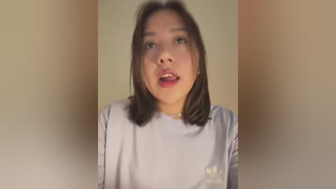 Media: A video of a young Asian woman with shoulder-length dark hair, light skin, and red lipstick, wearing a white shirt with a subtle logo, against a plain beige background.