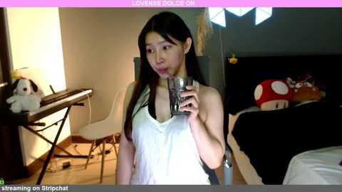 Media: A video shows a young Asian woman in a white tank top, drinking water in a room with a Super Mario plush toy and a white chair.