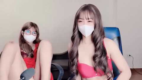 Media: Video of an Asian woman with long wavy brown hair, wearing a red bra and white mask, sitting on a blue chair.