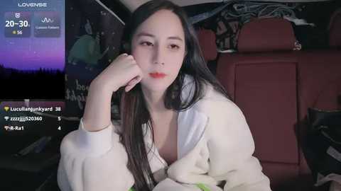 Media: Video of an East Asian woman with long black hair, fair skin, and red lipstick, wearing a white cardigan, resting her head on her hand in a dimly lit car.