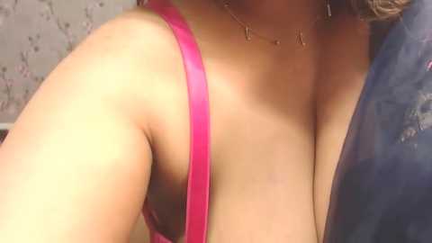 Video of a close-up of a woman's chest in a bright pink bra, with a necklace, blurry background.