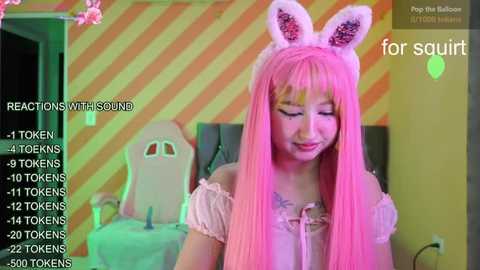 Media: A photo of a young Asian woman with long pink hair, wearing bunny ears and a frilly pink top, sitting in a striped room. Text overlays show reactions and number of tokens.