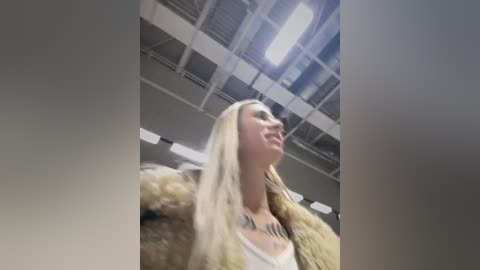 Media: A video captures a blonde woman with a fur coat and a tattoo on her chest, standing in a modern, dimly lit room with exposed ceilings and fluorescent lighting.