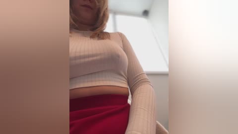 Media: A video of a light-skinned woman with blonde hair, wearing a white ribbed crop top and red skirt, taken from a low angle, emphasizing her midsection and breasts.