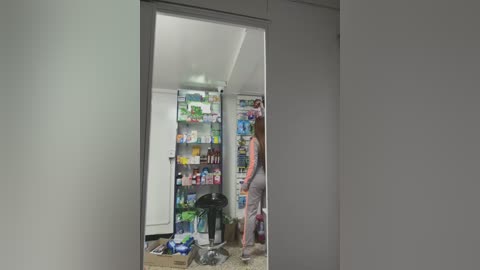 Media: Video of a small, cluttered kitchen with a white refrigerator and a person in a light shirt opening the fridge, surrounded by cardboard boxes and a plastic bag.