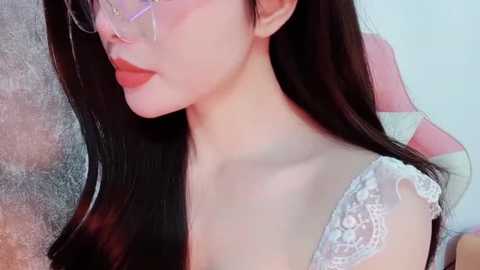 Media: Video of an East Asian woman with fair skin, long black hair, and light purple glasses, wearing a white lace bra. Background is a blurred mix of neutral colors.